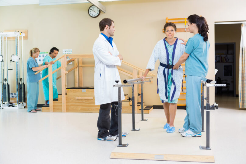Physical therapists assisting female patient in walking with the Physical therapists assisting female patient in walking with the support of handrails