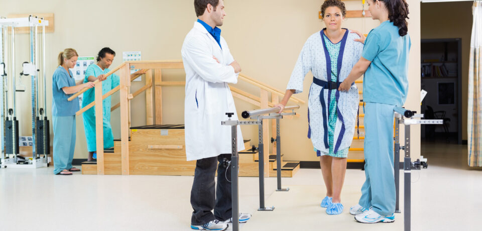 Physical therapists assisting female patient in walking with the support of handrails